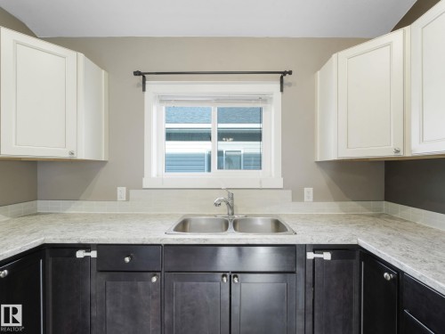 Kitchen featuring a double basin stainless steel sink, light countertops, and cabinetry with both light and dark finishes - 5035 51 Avenue, Lamont, AB - Indoor Photo Showing Kitchen With Double Sink