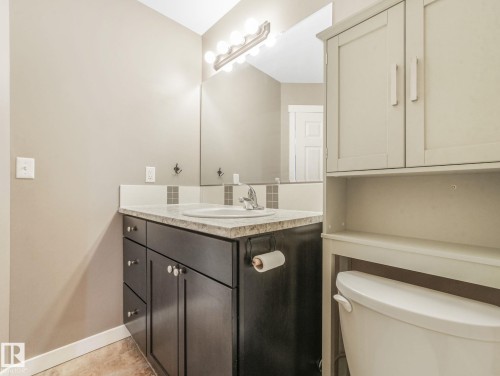 Bathroom featuring a vanity with dark wood cabinetry and a light-colored countertop, a mirror with overhead lighting, and an over-the-toilet storage unit - 5035 51 Avenue, Lamont, AB - Indoor Photo Showing Bathroom