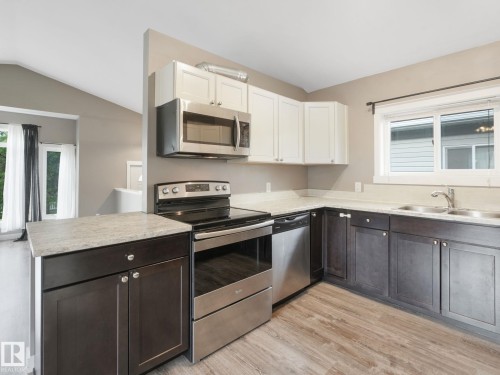 The kitchen features stainless steel appliances, dark lower cabinetry, light upper cabinetry, and light-colored countertops - 5035 51 Avenue, Lamont, AB - Indoor Photo Showing Kitchen With Stainless Steel Kitchen With Double Sink