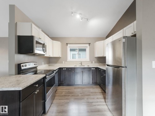 The kitchen features a U-shaped layout with light-colored countertops, dark lower cabinetry, and light upper cabinetry - 5035 51 Avenue, Lamont, AB - Indoor Photo Showing Kitchen With Stainless Steel Kitchen