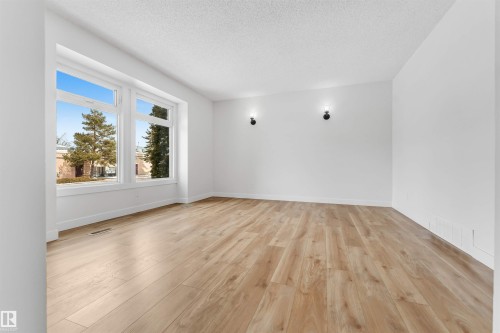 This spacious room features light-toned hardwood flooring and large windows, allowing for abundant natural light - 10865 21 Ave, Edmonton, AB - Indoor Photo Showing Other Room