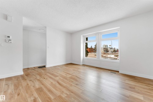 Bright living area featuring light-toned hardwood flooring and a large window providing views of the surrounding area - 10865 21 Ave, Edmonton, AB - Indoor