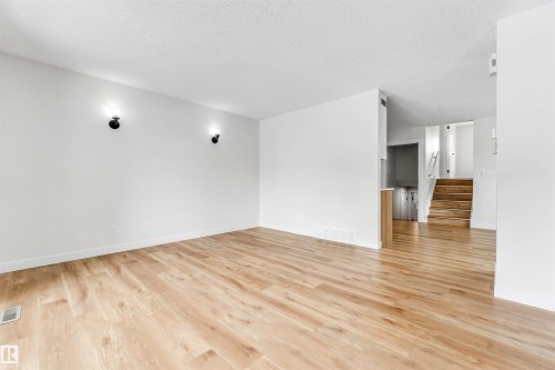 This expansive room features light-toned hardwood flooring and crisp white walls, illuminated by two wall-mounted sconces - 10865 21 Ave, Edmonton, AB - Indoor Photo Showing Other Room