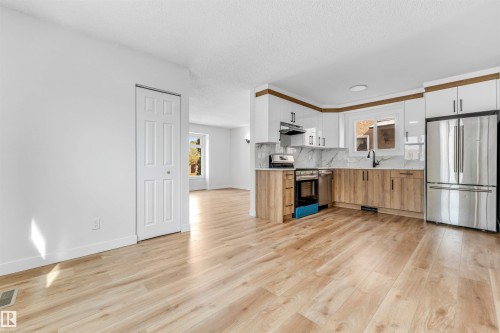 This bright space features light-toned flooring, white walls, and a modern kitchen with a stainless steel refrigerator and range - 10865 21 Ave, Edmonton, AB - Indoor Photo Showing Kitchen