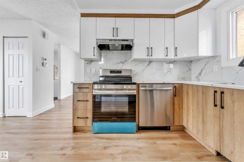 Well-appointed kitchen featuring a stainless steel oven and dishwasher, white upper cabinetry, light wood lower cabinetry, and a white marble-patterned backsplash - 10865 21 Ave, Edmonton, AB - Indoor Photo Showing Kitchen With Upgraded Kitchen