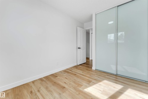This room features light-toned wood flooring, crisp white walls, and a white interior door with dark hardware - 10865 21 Ave, Edmonton, AB - Indoor Photo Showing Other Room