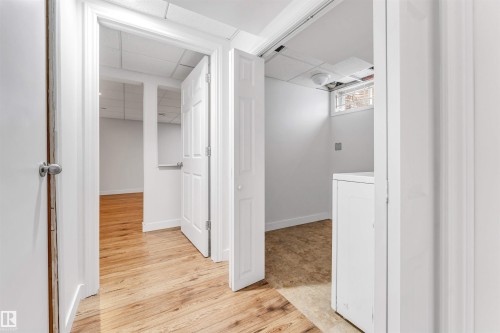 This interior hallway features wood-look flooring and white walls, leading to additional rooms with consistent flooring and white doors - 10865 21 Ave, Edmonton, AB - Indoor