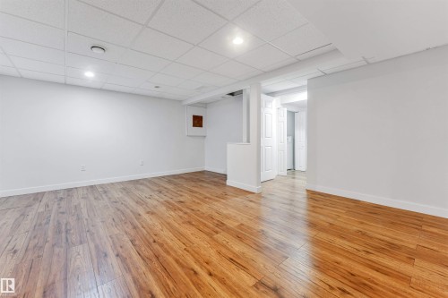 Spacious interior room featuring wood-style flooring, white walls, and a drop ceiling with recessed lighting - 10865 21 Ave, Edmonton, AB - Indoor Photo Showing Other Room