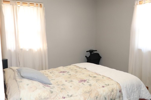 This room features light-colored walls and two windows with white curtains, providing natural light - 5512 50Th Ave, Wetaskiwin, AB - Indoor Photo Showing Bedroom