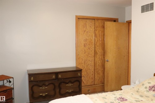 This room features light-colored walls, a wood dresser with decorative handles, and wood closet doors - 5512 50Th Ave, Wetaskiwin, AB - Indoor Photo Showing Bedroom