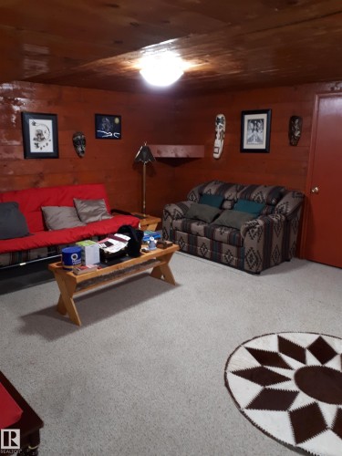 The property features a room with wood paneling on the ceiling and walls, carpeted floors, and a red interior door - 5512 50Th Ave, Wetaskiwin, AB - Indoor