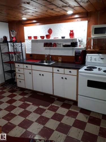 The property features a kitchen with a checkerboard floor, wooden paneled ceiling, white cabinetry, and a white oven - 5512 50Th Ave, Wetaskiwin, AB - Indoor Photo Showing Kitchen