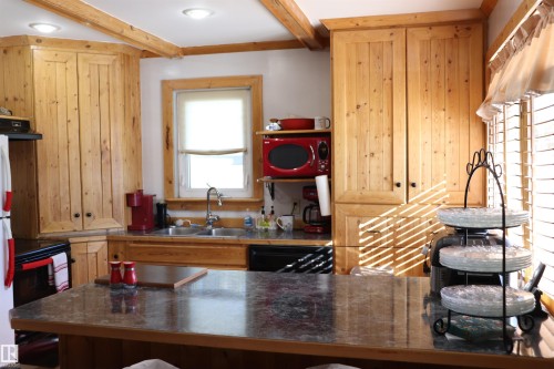 The kitchen features wood cabinetry, a double basin sink, and an island with a dark countertop - 5512 50Th Ave, Wetaskiwin, AB - Indoor Photo Showing Kitchen With Double Sink