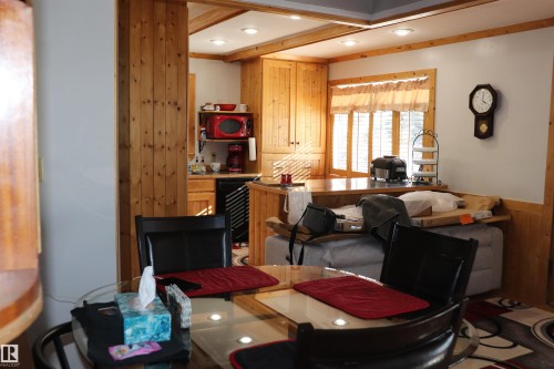 The property features wood paneling and cabinetry, a kitchen with a window and bar-style counter, and a dining area with a glass-top table - 5512 50Th Ave, Wetaskiwin, AB - Indoor