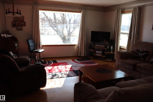 Living area featuring hardwood flooring, natural light through large windows, and a decorative area rug - 5512 50Th Ave, Wetaskiwin, AB - Indoor Photo Showing Living Room