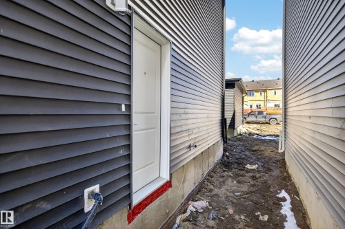 Exterior entrance featuring a white door, dark horizontal siding, an exterior light fixture, and a foundational base - 408 Crystal Creek Link, Leduc, AB - Outdoor With Exterior
