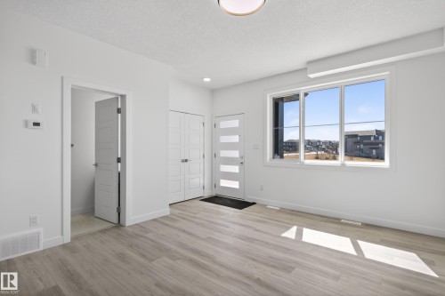 Bright entryway featuring wood-finish flooring, a modern glass-paneled front door, a large picture window, and a convenient coat closet - 408 Crystal Creek Link, Leduc, AB - Indoor Photo Showing Other Room