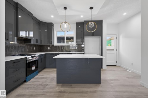 Modern kitchen featuring sleek grey cabinetry, light-toned wood-finish flooring, and a stone-finish backsplash - 408 Crystal Creek Link, Leduc, AB - Indoor Photo Showing Kitchen With Upgraded Kitchen