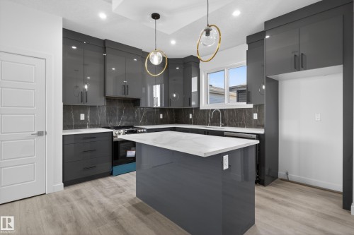 Modern kitchen featuring glossy dark gray cabinetry, a central island with a light-toned countertop, and wood-finish flooring - 408 Crystal Creek Link, Leduc, AB - Indoor Photo Showing Kitchen With Upgraded Kitchen