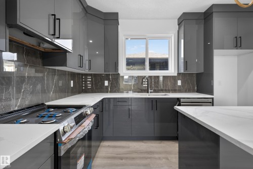 Contemporary kitchen featuring dark gray cabinetry with black hardware, white countertops, a gas range, a stainless steel sink with a high-arc faucet, and dark gray slab backsplash - 408 Crystal Creek Link, Leduc, AB - Indoor Photo Showing Kitchen