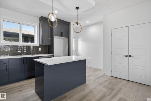 Kitchen featuring a dark blue island with a white countertop, coordinating cabinetry, and a dark marble-look backsplash - 408 Crystal Creek Link, Leduc, AB - Indoor Photo Showing Kitchen