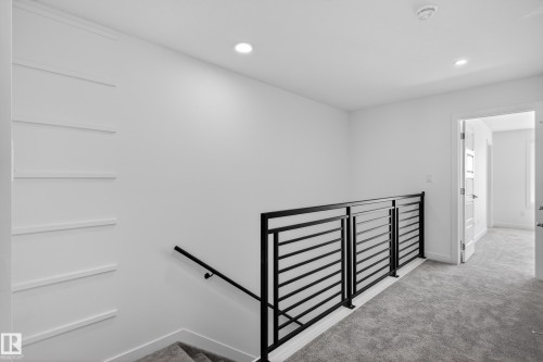 Contemporary black horizontal bar railing, recessed ceiling lighting, textured gray carpeting, white painted walls, and a white paneled door - 408 Crystal Creek Link, Leduc, AB - Indoor Photo Showing Other Room