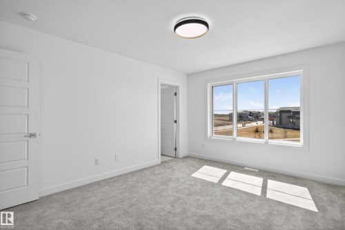 Light-filled room featuring a large triple-pane window, neutral carpet flooring, a contemporary flush-mount ceiling light fixture, and white trim throughout - 408 Crystal Creek Link, Leduc, AB - Indoor Photo Showing Other Room