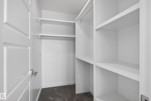Walk-in closet featuring built-in shelving, hanging rods, and dark gray carpeting - 408 Crystal Creek Link, Leduc, AB - Indoor With Storage