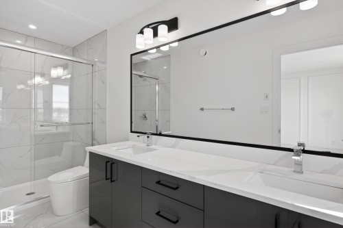 Modern bathroom featuring a dual vanity with dark cabinetry, integrated rectangular sinks, and a large mirror with contemporary lighting - 408 Crystal Creek Link, Leduc, AB - Indoor Photo Showing Bathroom