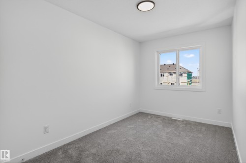 Bright room featuring neutral walls, grey carpeting, a flush-mount ceiling light, and a white-framed window - 408 Crystal Creek Link, Leduc, AB - Indoor Photo Showing Other Room