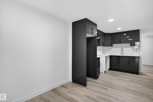 Contemporary kitchen featuring dark cabinetry, white countertops, a matching white tile backsplash, and light wood-finish flooring - 408 Crystal Creek Link, Leduc, AB - Indoor