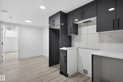 Contemporary kitchen area featuring dark cabinetry, white countertops, and a white tile backsplash with gray veining - 408 Crystal Creek Link, Leduc, AB - Indoor