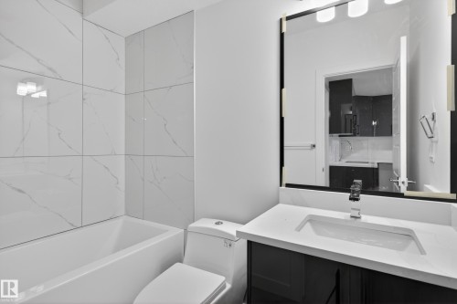 Bathroom featuring a white subway-tiled bathtub surround, a built-in bathtub, a white toilet, a dark wood-finish vanity with a white countertop, and an integrated sink with a chrome faucet - 408 Crystal Creek Link, Leduc, AB - Indoor Photo Showing Bathroom