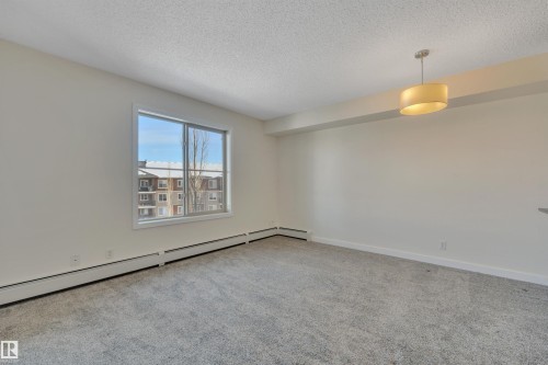 This living space features light-colored walls, grey carpet flooring, and a large window providing views of the exterior - 415 12035 22 Avenue, Edmonton, AB - Indoor Photo Showing Other Room