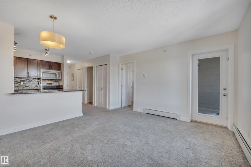Open concept living area featuring light gray carpeting, white walls, and a modern drum pendant light fixture - 415 12035 22 Avenue, Edmonton, AB - Indoor Photo Showing Other Room