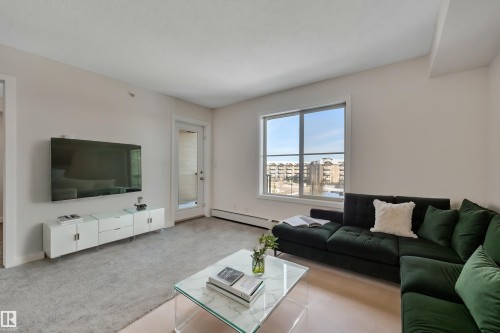 Living area featuring light-colored walls, a large window, a glass sliding door, and light-colored flooring - 415 12035 22 Avenue, Edmonton, AB - Indoor Photo Showing Living Room