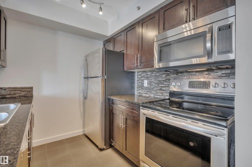 The kitchen features dark wood cabinetry, stainless steel appliances, and granite countertops - 415 12035 22 Avenue, Edmonton, AB - Indoor Photo Showing Kitchen
