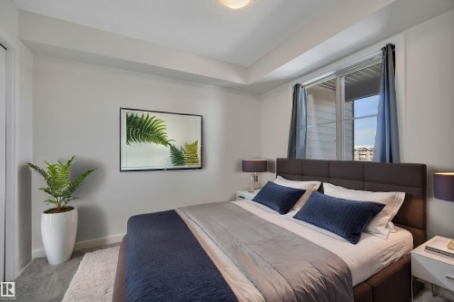 The bedroom features a window with blue curtains, a textured headboard, and light grey walls - 415 12035 22 Avenue, Edmonton, AB - Indoor Photo Showing Bedroom