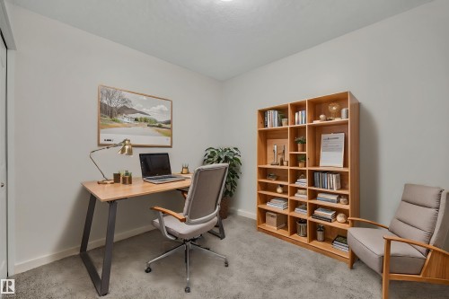 This versatile room features light gray walls, plush gray carpeting, and a built-in wooden shelving unit, offering a flexible space for various uses - 415 12035 22 Avenue, Edmonton, AB - Indoor Photo Showing Office