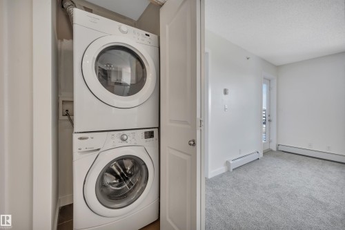 The property includes a stacked washer and dryer unit, and a room with light grey carpeting, white walls, and a door leading to an exterior space - 415 12035 22 Avenue, Edmonton, AB - Indoor Photo Showing Laundry Room