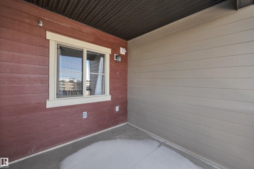 This property features a covered patio with a textured ceiling, a window with exterior trim, and exterior wall lighting - 415 12035 22 Avenue, Edmonton, AB - Outdoor With Exterior