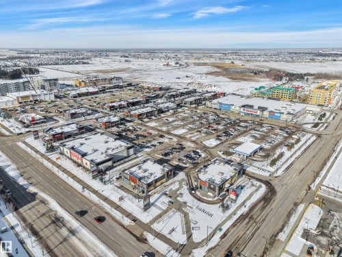 Aerial view of the property's surrounding commercial district, featuring various retail buildings, paved parking lots, and roadways - 415 12035 22 Avenue, Edmonton, AB - Outdoor With View