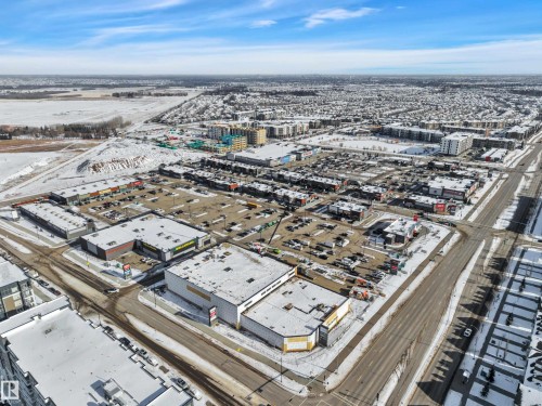 Aerial view of the surrounding area featuring commercial buildings with parking lots, residential buildings, and open land - 415 12035 22 Avenue, Edmonton, AB - Outdoor With View