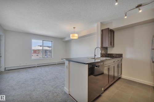 Open concept living space featuring a kitchen island with a dark countertop, an integrated sink, and stainless steel appliances - 415 12035 22 Avenue, Edmonton, AB - Indoor Photo Showing Kitchen