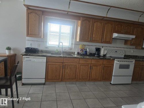 The kitchen features wood cabinetry, a window with blinds, a white dishwasher, and a white range - Edmonton, AB - Indoor Photo Showing Kitchen
