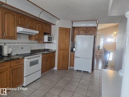 The kitchen features wood cabinetry, a white tile backsplash, and a white refrigerator and oven - Edmonton, AB - Indoor Photo Showing Kitchen