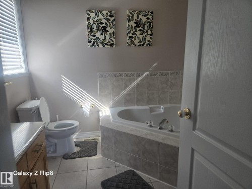 The bathroom features a corner soaking tub with tiled surround, a toilet, and a window with horizontal blinds - Edmonton, AB - Indoor Photo Showing Bathroom