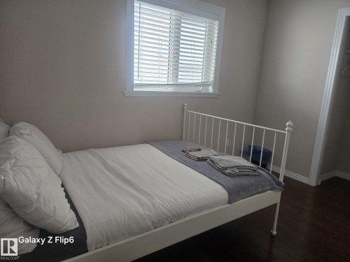 This room features a window with blinds, dark flooring, and light-colored walls - Edmonton, AB - Indoor Photo Showing Bedroom