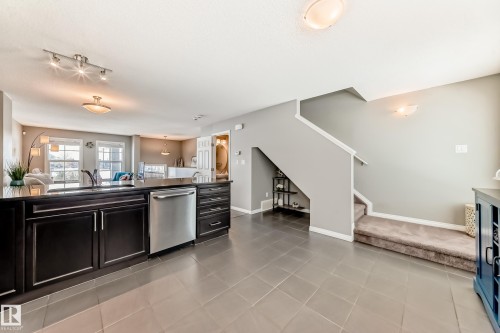 The kitchen features dark cabinetry, a stainless steel dishwasher, and a black countertop - 86 4029 Orchards Drive, Edmonton, AB - Indoor Photo Showing Other Room