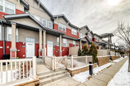 The property features a row of multi-level townhomes with red and grey siding, white doors, and front porches - 86 4029 Orchards Drive, Edmonton, AB - Outdoor With Facade